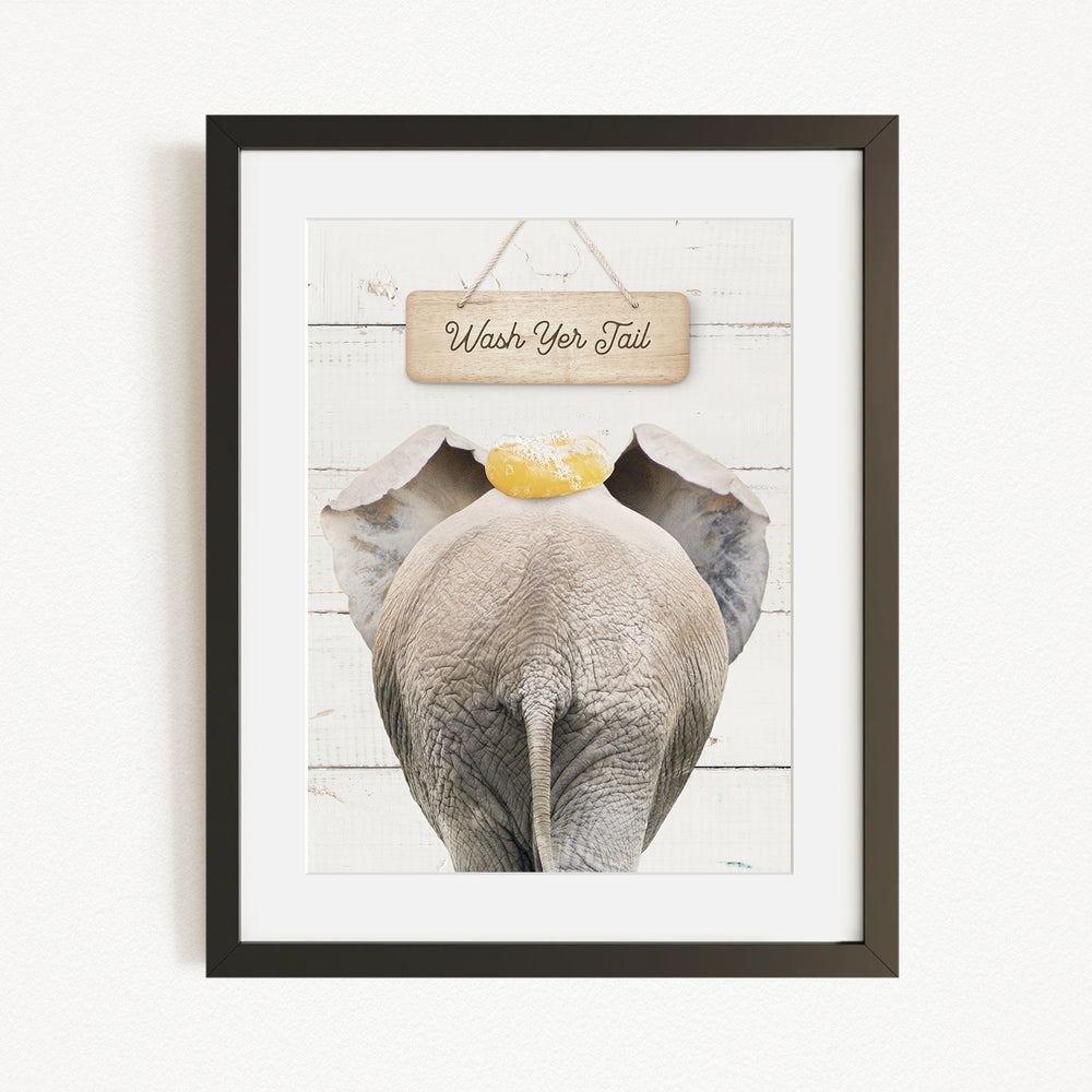 A framed image of an elephant with a sign that says "Wash Your Tail" hanging above it.
