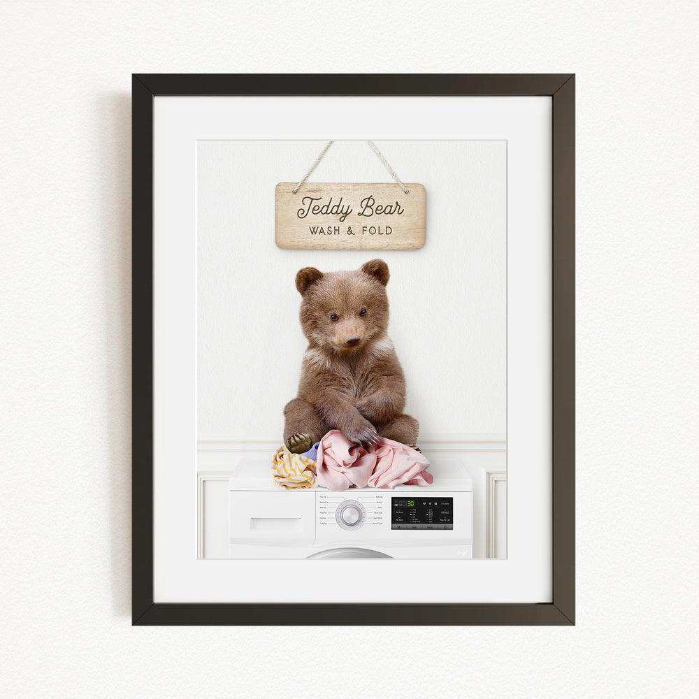 A framed image of a teddy bear sitting on a washing machine, with a sign above it that says "Teddy Bear Wash & Fold".