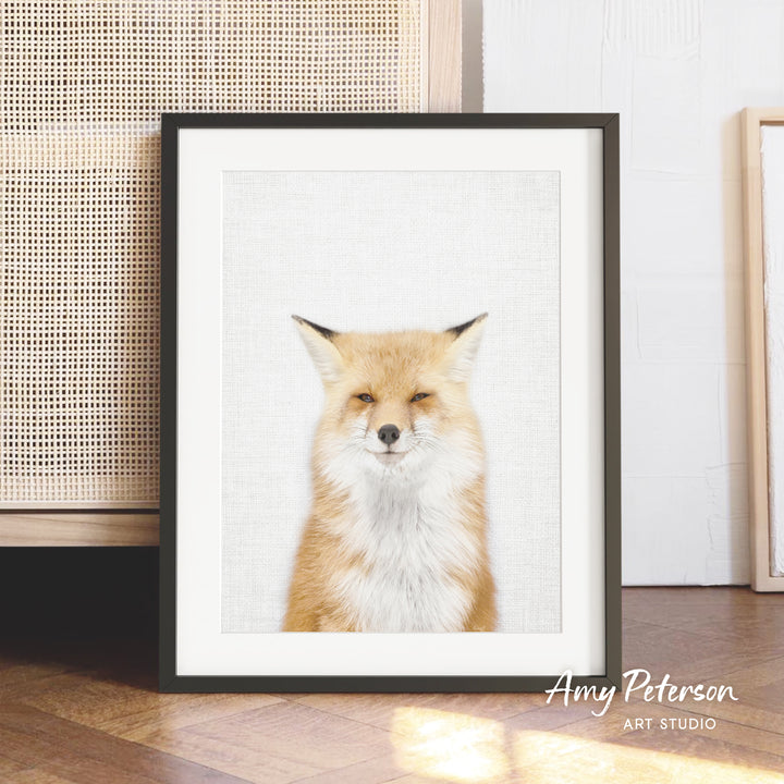 A framed photograph of a smiling orange fox is displayed on a wooden floor in front of a woven basket.