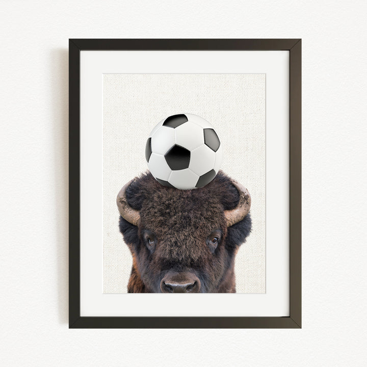 A framed image of a bison with a soccer ball on its head.