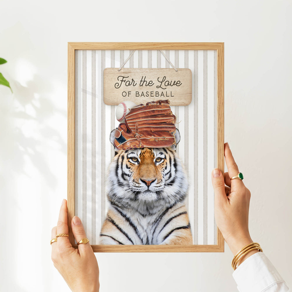 A person's hands are holding a framed picture of a tiger wearing a baseball cap and glove, with a sign above the picture that says "For the Love of Baseball".