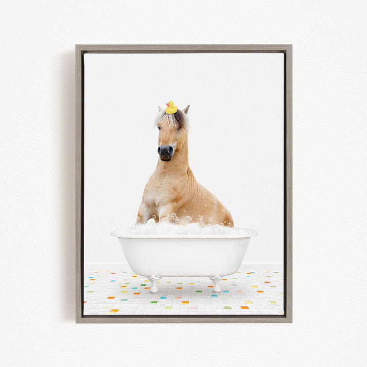 A light brown horse is sitting in a white bathtub filled with bubbles, with a yellow rubber duck perched on its head.