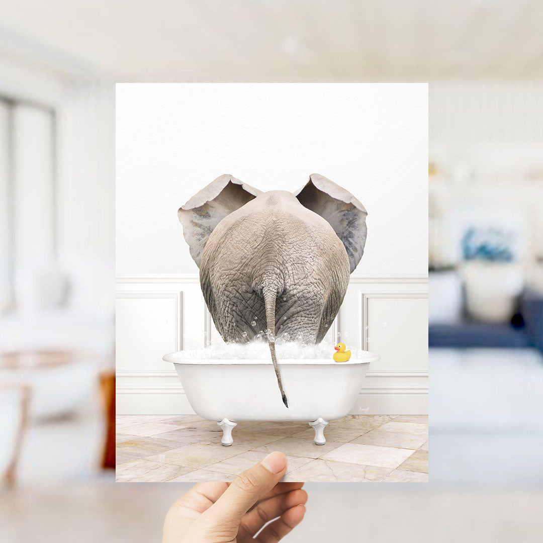 A hand holds up a framed image of an elephant standing in a bathtub filled with water and a rubber duck.