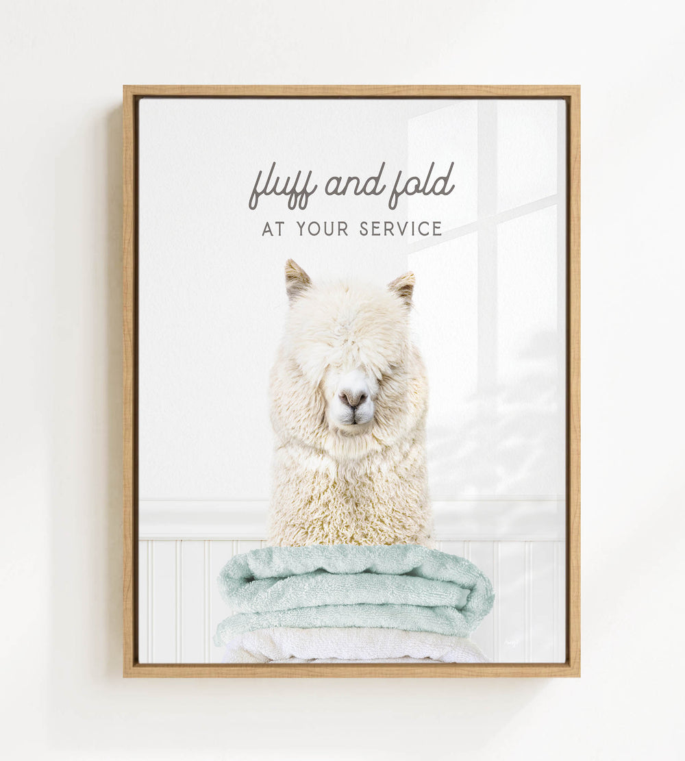 A fluffy white alpaca sitting on a stack of light blue towels, with the text "fluff and fold at your service" written above the image.
