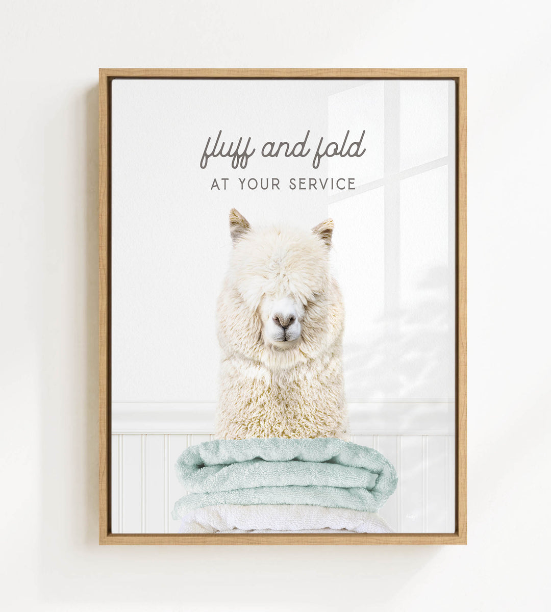 A fluffy white alpaca sitting on a stack of light blue towels, with the text "fluff and fold at your service" written above the image.