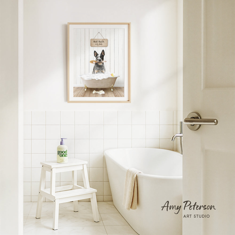 A framed image of a dog sitting in a bathtub, with a sign above it that says "Hot bath $1.00". The image is set in a bathroom with a white bathtub, a stool, and a towel.