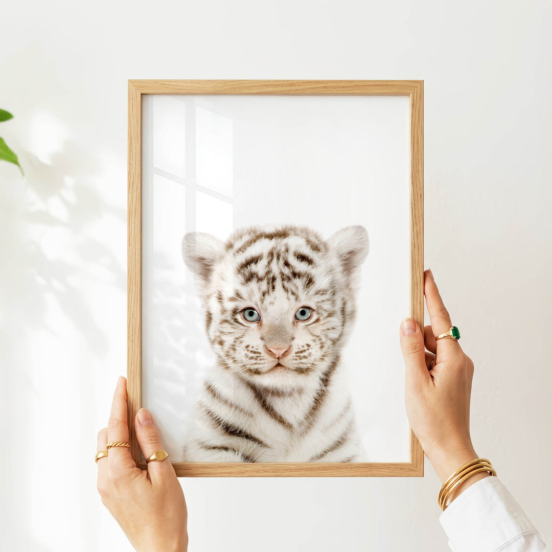 A person's hands are holding a wooden frame with a picture of a young tiger inside it.
