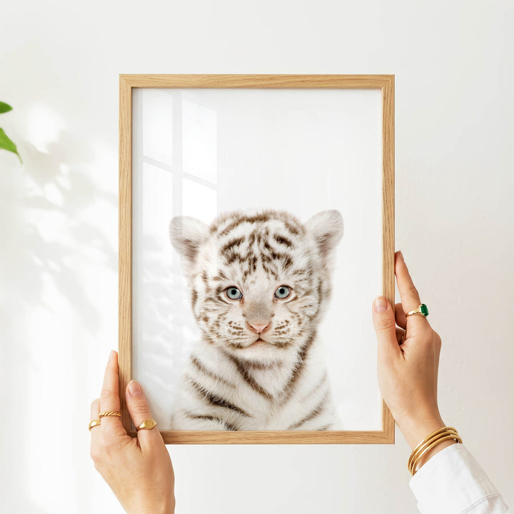 A person's hands are holding a wooden frame with a picture of a young tiger inside it.
