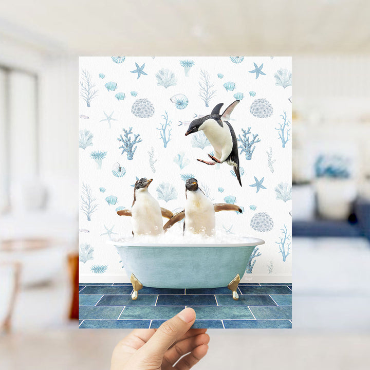 A hand holds up a framed image depicting two penguins sitting in a bathtub, surrounded by a blue and white ocean-themed background.