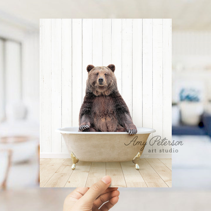 a hand holding a photo of a bear in a bathtub