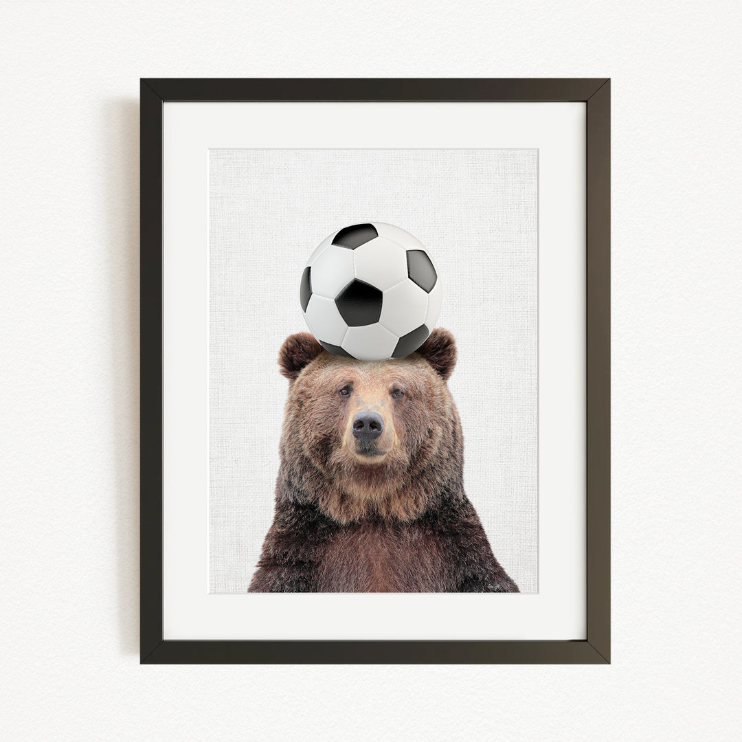 A brown bear balancing a soccer ball on its head.