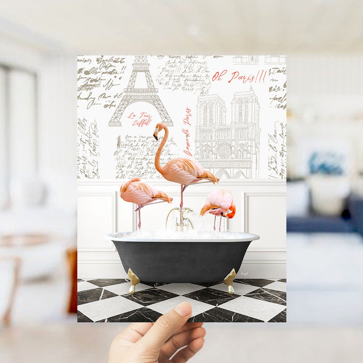 A hand is holding up a framed image featuring three flamingos sitting in a bathtub, with the Eiffel Tower and other Parisian landmarks visible in the background.
