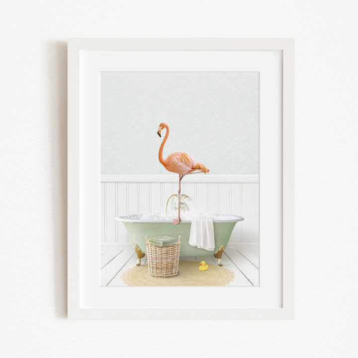 A framed image depicting a pink flamingo standing on the edge of a green bathtub, with a basket of bath toys and a yellow rubber duck nearby.