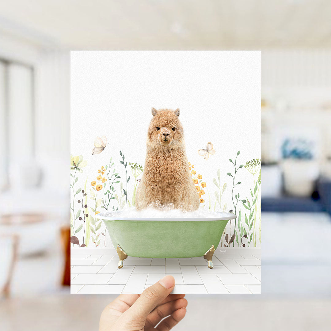 A hand holds up a framed image of a fluffy brown alpaca sitting in a green bathtub filled with bubbles, surrounded by a floral and butterfly-themed background.