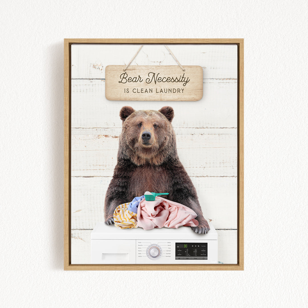 A framed image of a brown bear sitting on a washing machine, with a sign above that says "Bear Necessity is Clean Laundry".
