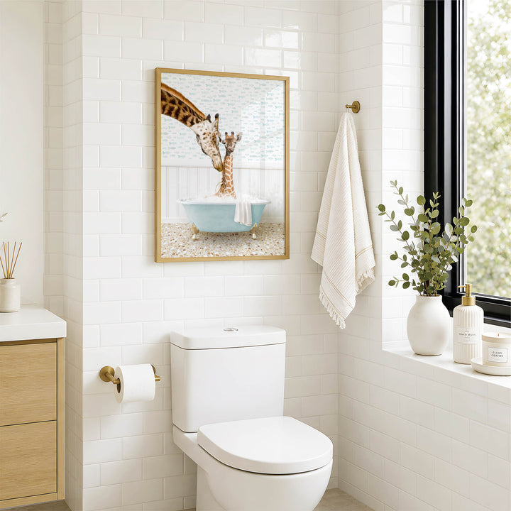 A bathroom with a white toilet, a framed picture of two giraffes in a bathtub, and a window with greenery on the sill.