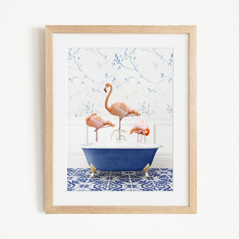 A framed image depicting three flamingos standing in a blue bathtub, with a patterned tile floor and a floral wallpaper in the background.