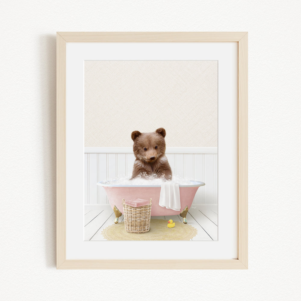 A cute brown bear sitting in a pink bathtub filled with bubbles, surrounded by a yellow rubber duck and a basket.