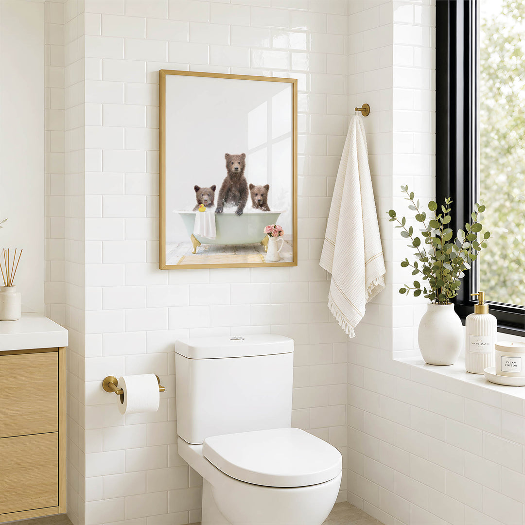 A bathroom with a white toilet, a framed picture of three bears sitting in a bathtub, and a window with greenery outside.