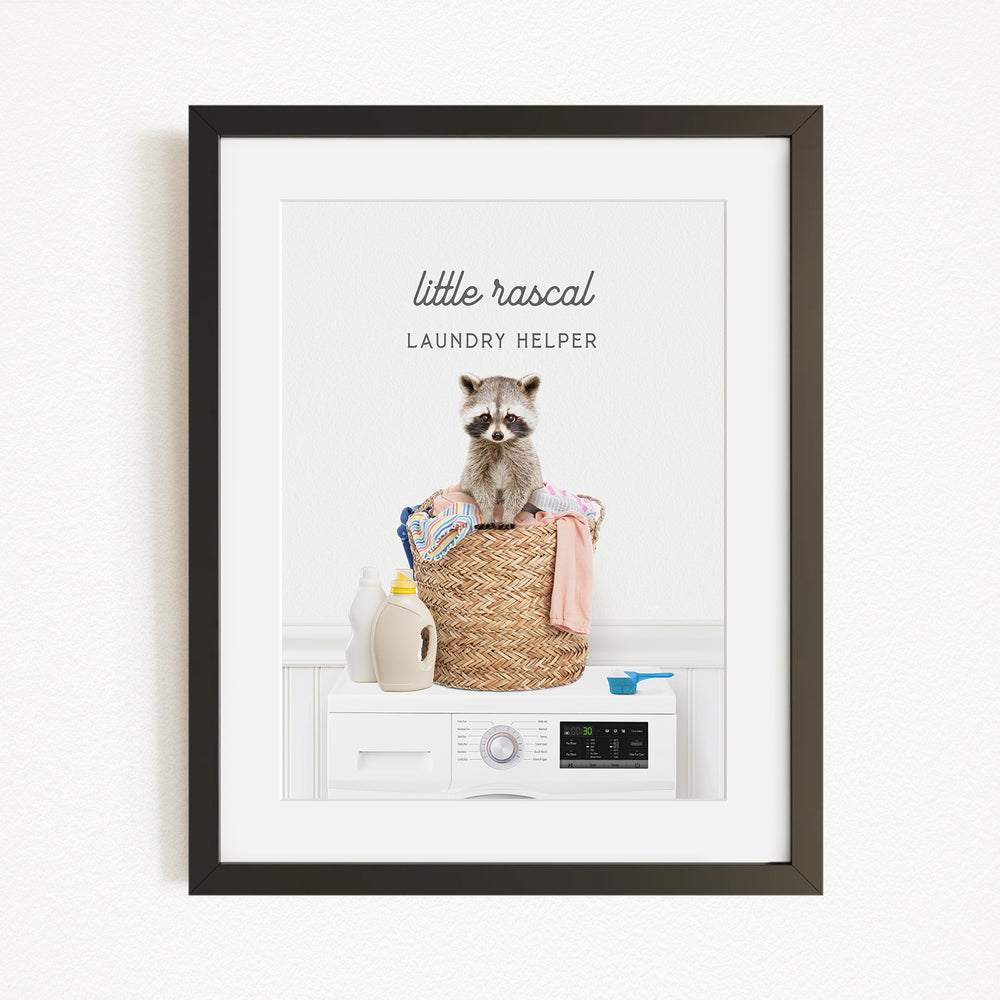 A raccoon sitting in a laundry basket filled with clothes and detergent, with a washing machine nearby.