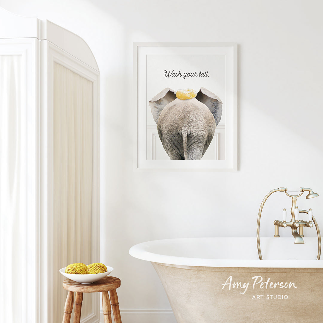 a bathroom with a framed elephant image on the wall, a wooden stool with a bowl of fruit, and a clawfoot bathtub with a faucet.
