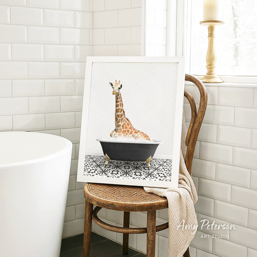 A framed image of a giraffe sitting in a bathtub is displayed on a wooden chair in a bathroom setting.