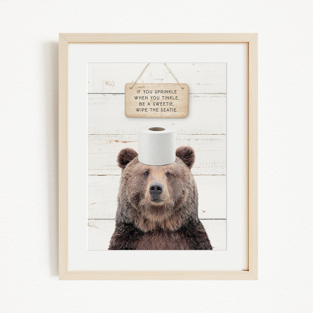 A framed image of a brown bear with a sign above its head that reads "If you sprinkle when you tinkle, be a twinkle, wipe the seattle."