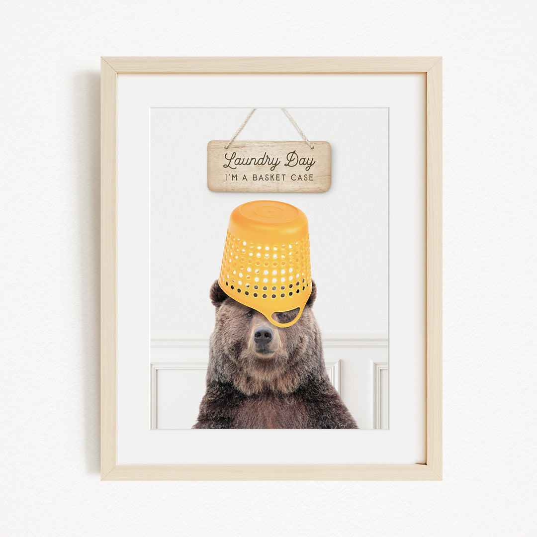 A framed image of a bear wearing a yellow basket hat, with a sign above it that says "Laundry Day I'm a basket case".