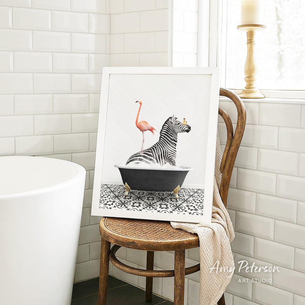 A framed image of a zebra sitting in a bathtub, with a pink flamingo standing on its back, is displayed on a wooden chair in a bathroom setting.