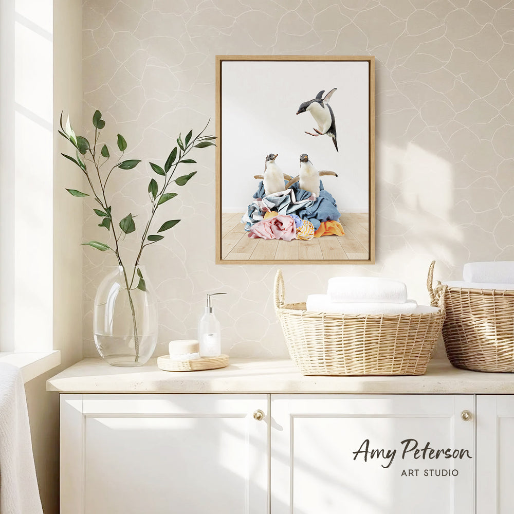 a framed painting of penguins on a wall, with a wicker basket and a vase of greenery on a counter below it.
