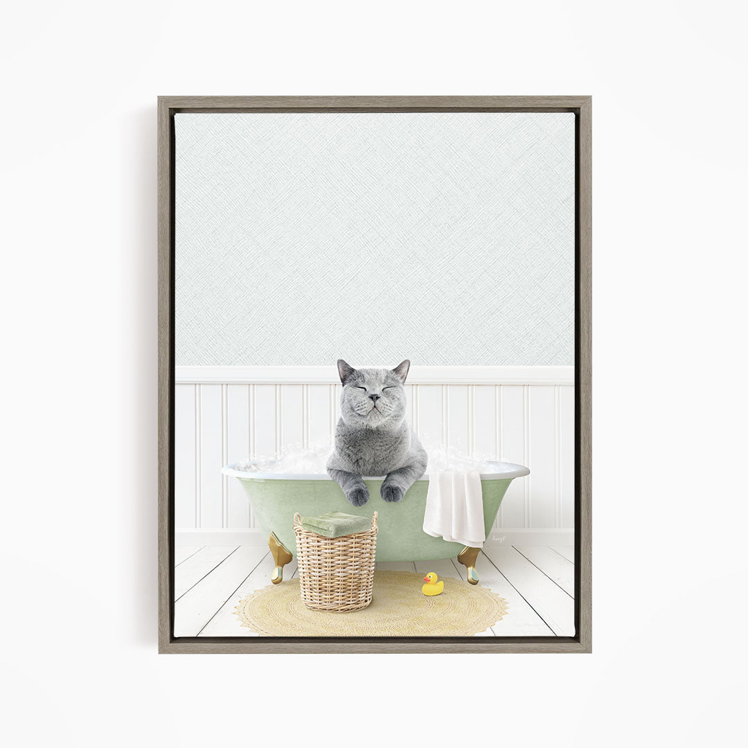 A gray cat sitting in a green bathtub filled with bubbles, surrounded by a yellow rubber duck and a woven basket.