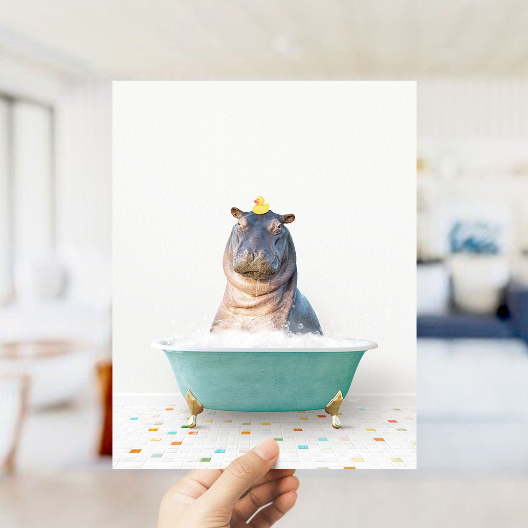 A hand holds up a framed image of a hippopotamus sitting in a bathtub, with a yellow rubber duck perched on its head.