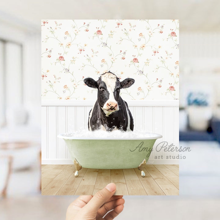 a hand holding up a photo of a cow in a bathtub