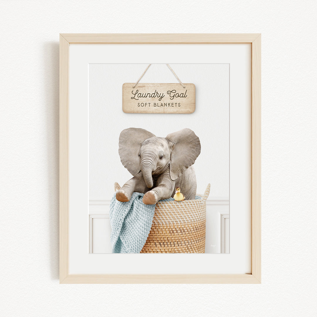 A framed image of an elephant sitting in a woven basket, with a sign above it that reads "Laundry Blankets".