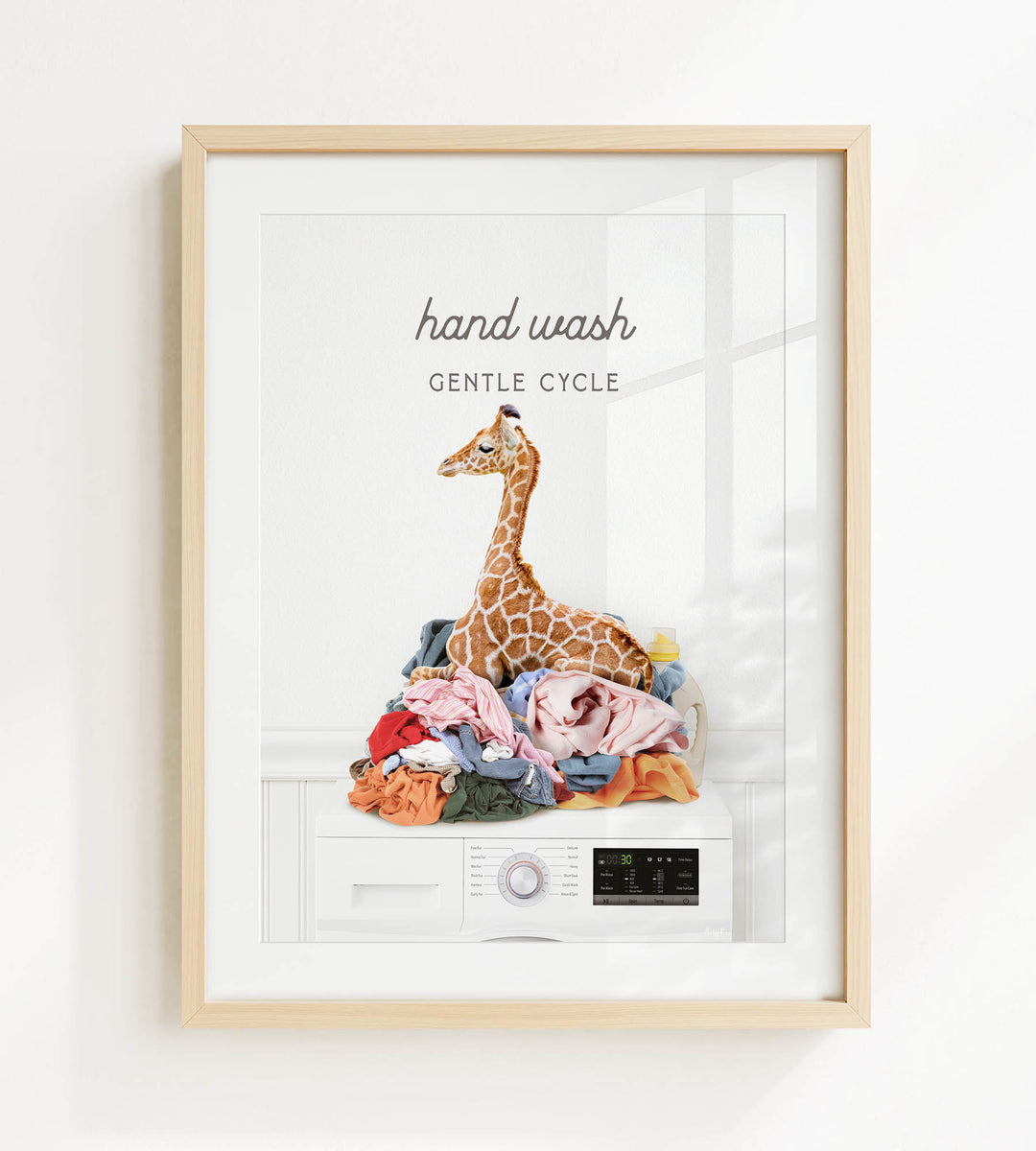 A framed image depicting a giraffe sitting on a pile of laundry, with the text "hand wash gentle cycle" above it.