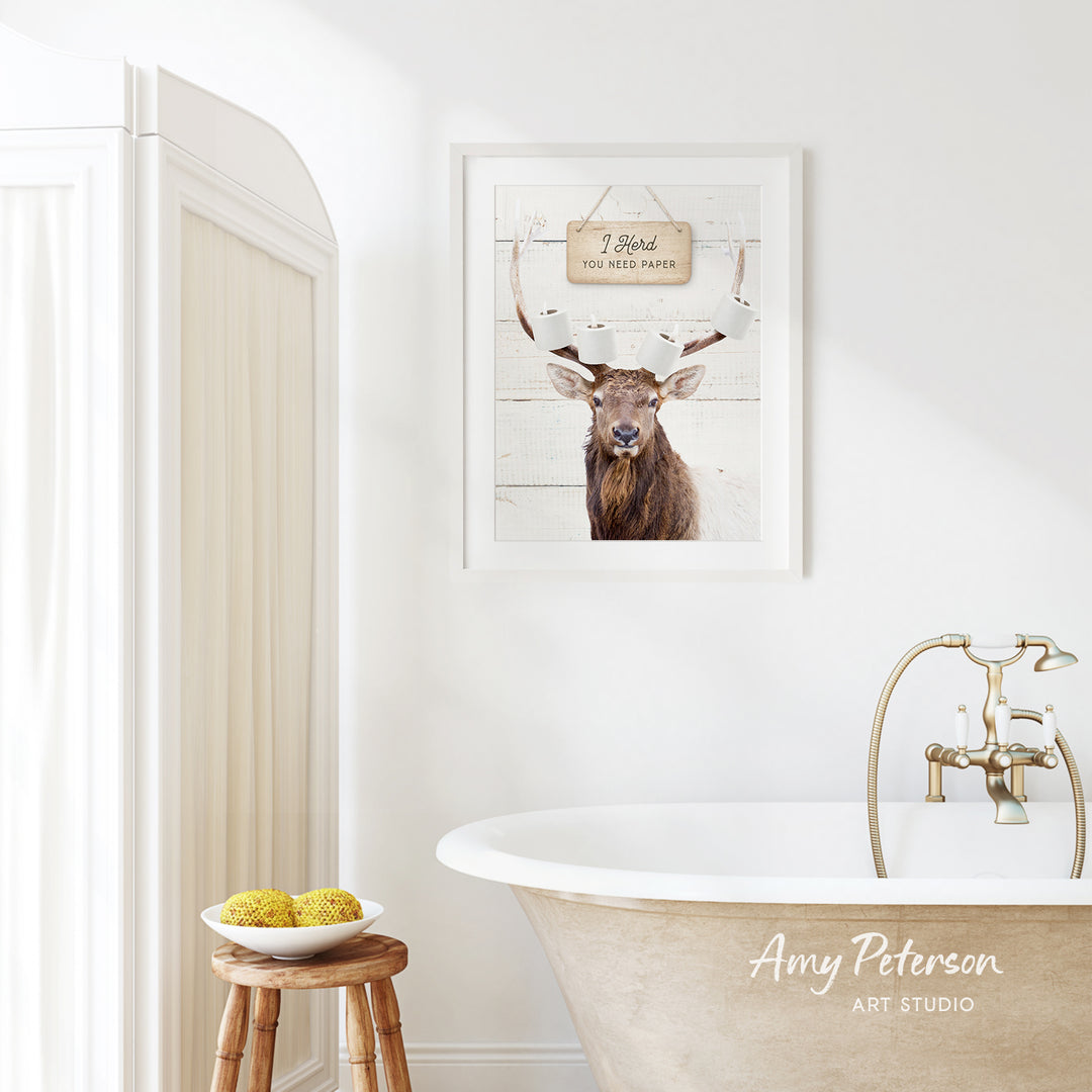 a bathroom with a framed picture of a deer with antlers, a wooden stool, a bowl of fruit, and a bathtub with a faucet.