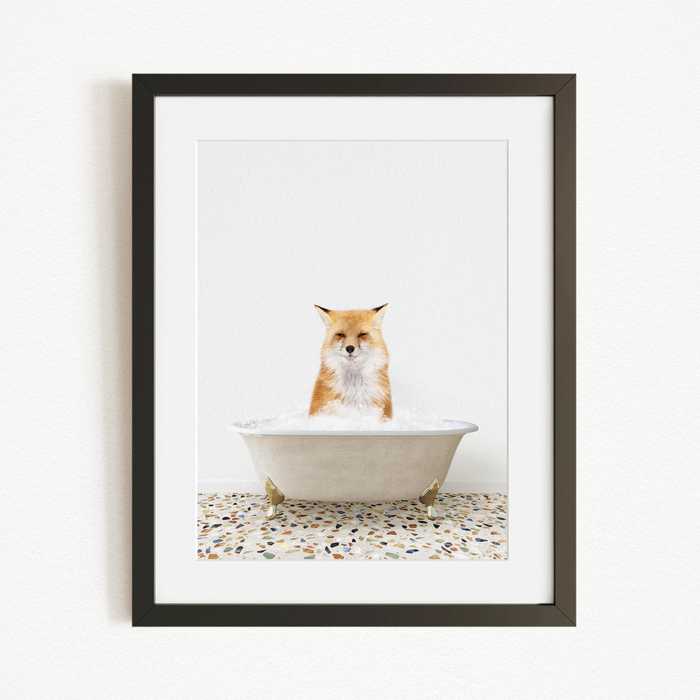 A red fox sitting in a white bathtub filled with bubbles, looking directly at the camera.