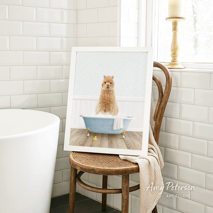 A framed image of a small brown dog sitting in a blue bathtub, surrounded by white tiles, is displayed on a wooden chair in a bathroom setting.