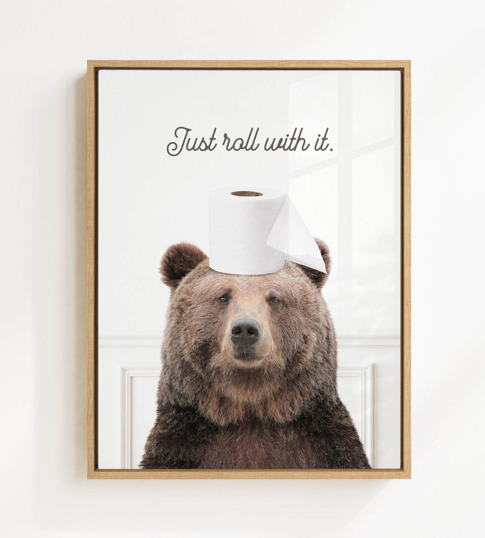A framed image of a brown bear wearing a roll of toilet paper on its head, with the text "Just roll with it."