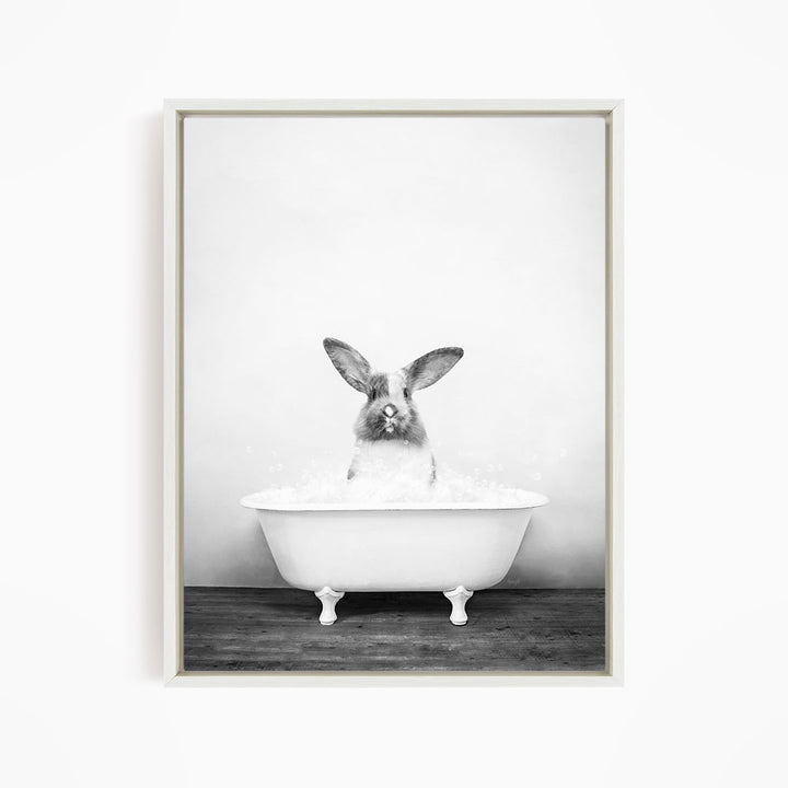 A rabbit sitting in a white bathtub filled with water, looking directly at the camera.
