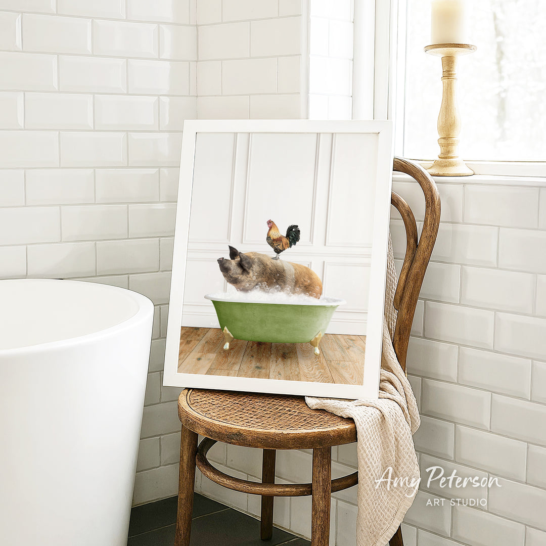 A framed image of a cat sitting in a green bathtub, with a rooster perched on its back, is displayed on a wooden chair in a bathroom setting.