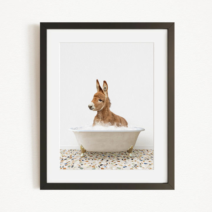 A donkey is sitting in a white bathtub filled with water, surrounded by a speckled floor.