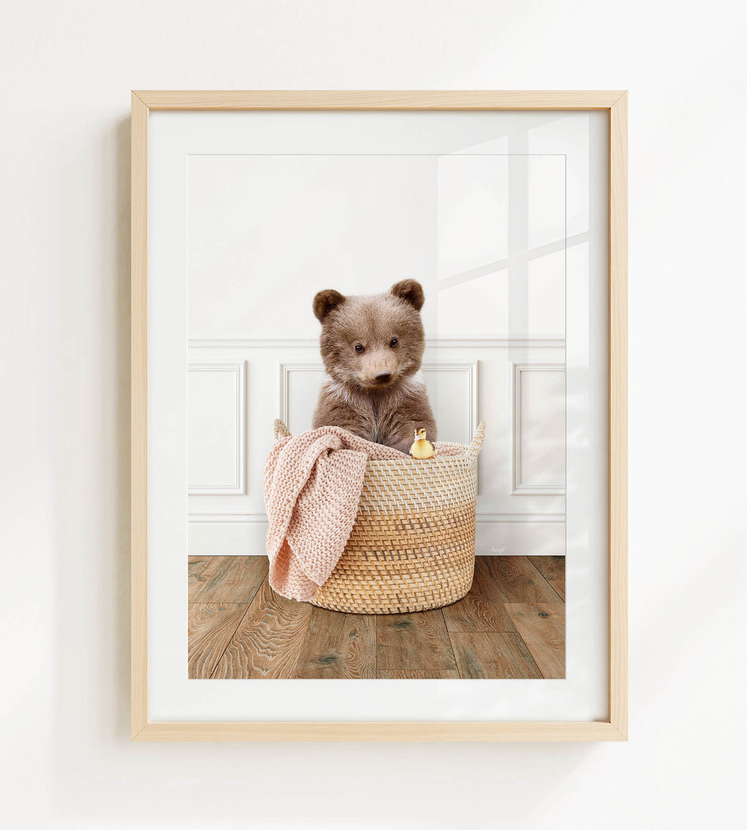 A brown bear sitting in a woven basket, with a pink blanket and a small toy duck nearby.