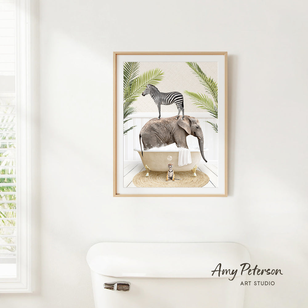 A framed illustration of a zebra and an elephant sitting together in a bathtub, surrounded by palm leaves, is displayed on a white wall.