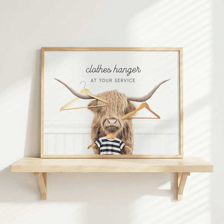 A framed image of a long-haired, horned animal holding clothes hangers, with the text "clothes hanger at your service" displayed above it.