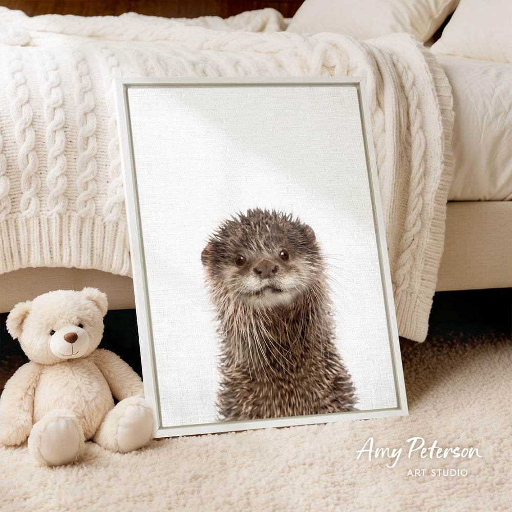A framed image of an otter is displayed on a white bedspread, accompanied by a teddy bear on the floor.