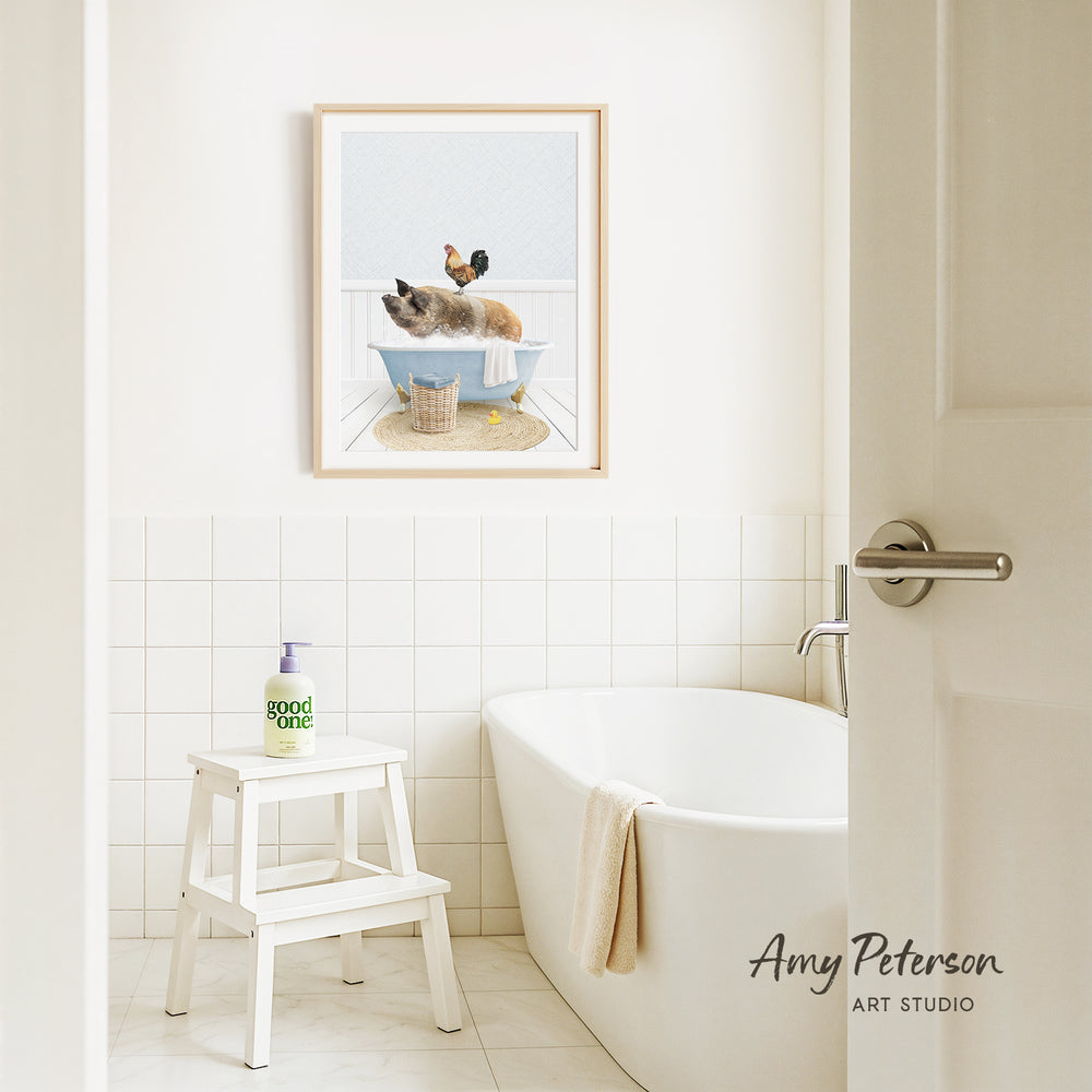 A framed image of a cat sitting in a bathtub is displayed on the wall above a white bathtub in a bathroom.