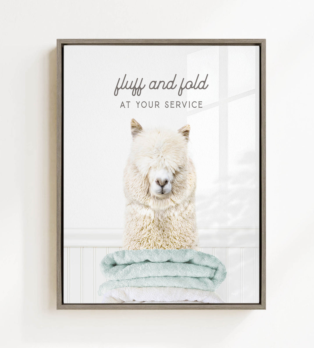 A fluffy white alpaca sitting on a stack of light blue towels, with the text "fluff and fold at your service" written above the image.