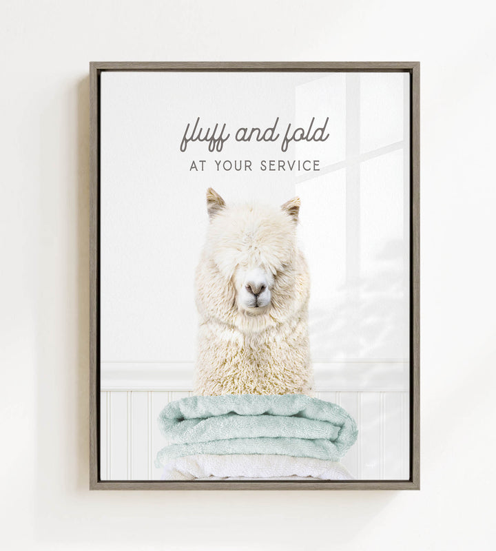 A fluffy white alpaca sitting on a stack of light blue towels, with the text "fluff and fold at your service" written above the image.