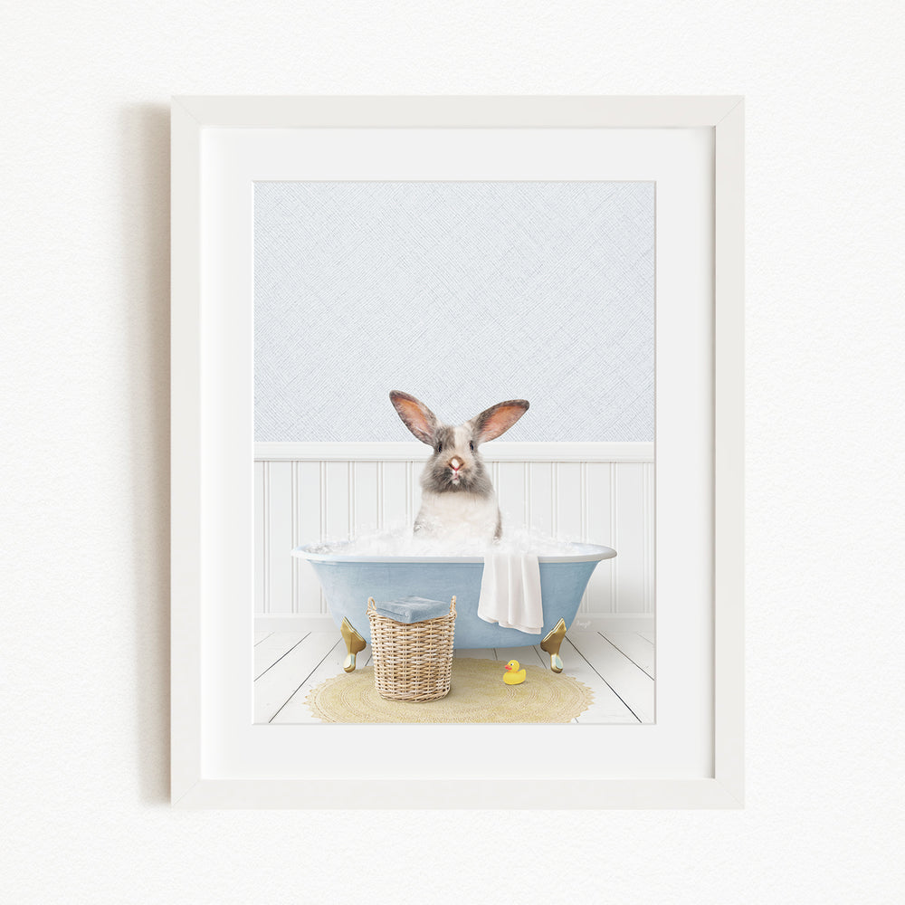 A white rabbit sitting in a blue bathtub filled with bubbles, surrounded by a yellow rubber duck and a basket.